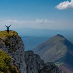 A person celebrating victory atop a mountain peak in Serbia with breathtaking views.